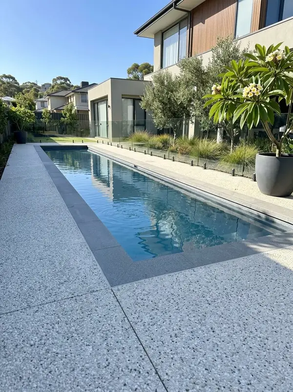 Pale exposed aggregate surround around a rectangular pool with a glass fence, Burnside
