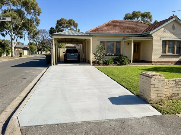 Single-width broom-finished concrete driveway beside a 1950s brick home