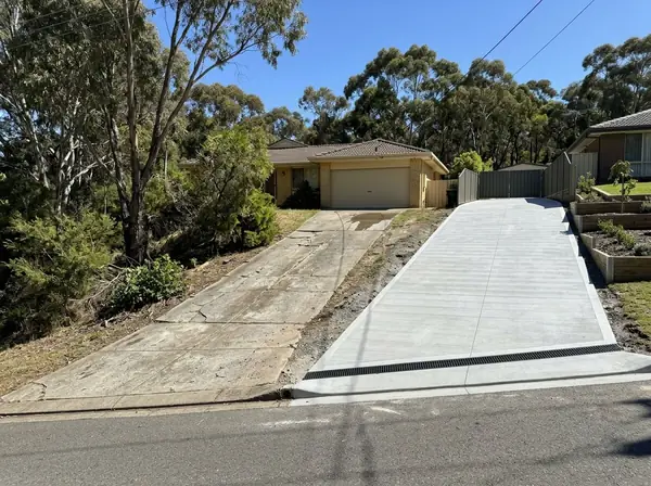 An old cracked sloping driveway beside a neighbour's new broom-finished drive with a strip drain, Golden Grove