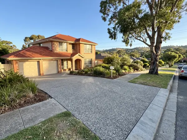 A new exposed aggregate double driveway sloping up to a 1990s two-storey brick veneer home in Golden Grove