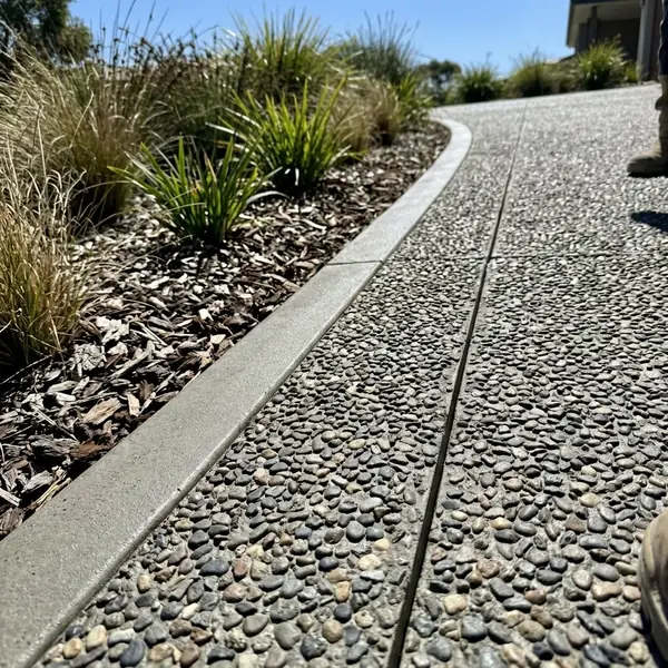 Close up of a new exposed aggregate driveway edge against a native garden bed