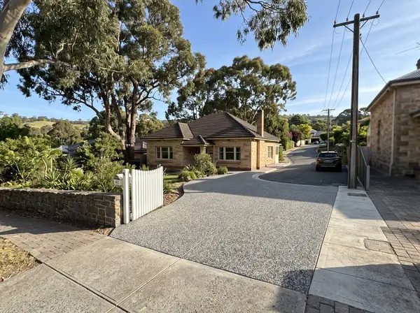 A new exposed aggregate driveway climbing to a 1930s sandstone bungalow under huge gum trees on a winding street in Mitcham
