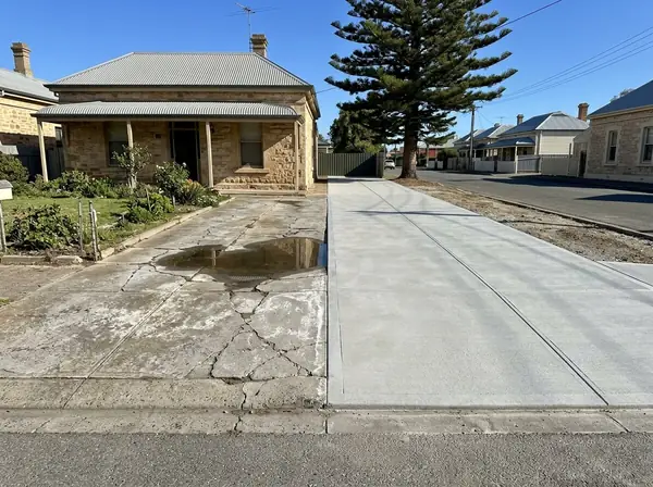 An old sunken, salt-stained cottage driveway beside a neighbour's new broom-finished one on a flat Port Adelaide street