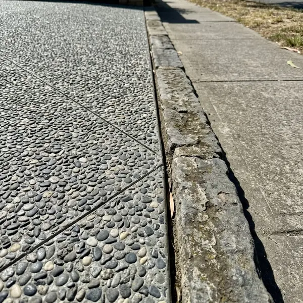 Close up of a new exposed aggregate driveway edge against an old bluestone kerb