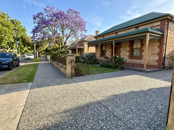 A new exposed aggregate driveway beside a sandstone villa with a return verandah on a leafy street in Prospect