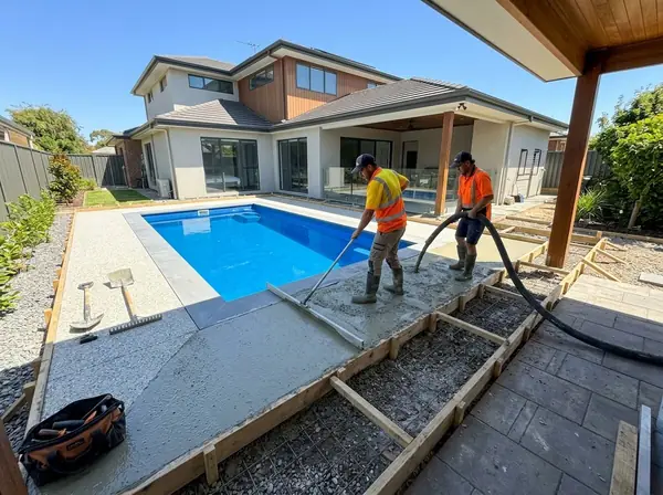 Two concreters pouring and screeding concrete around a newly installed fibreglass pool