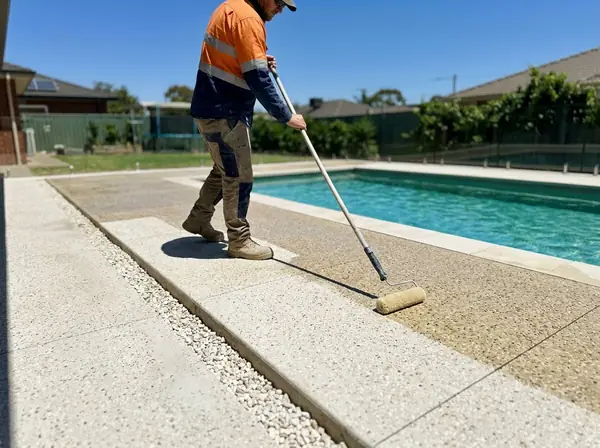 Rolling a non-slip sealer onto a pale pool surround