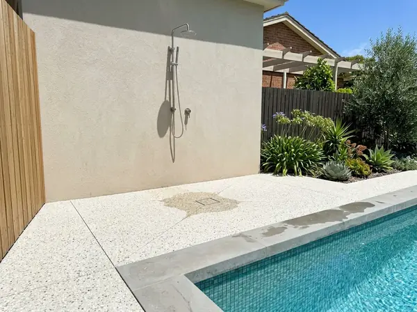 An outdoor shower with an exposed aggregate base draining to a grate