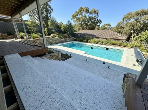 Wide exposed aggregate steps leading down from an alfresco to a pool surround