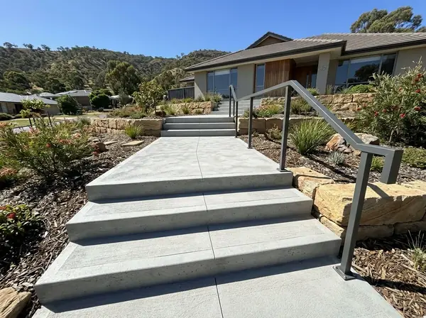 Broad concrete steps and a landing with a handrail on a sloped front yard