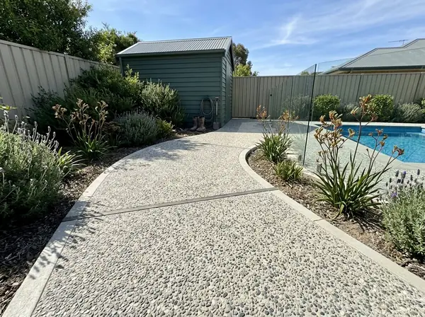 Pale exposed aggregate path around a pool fence to a pool shed