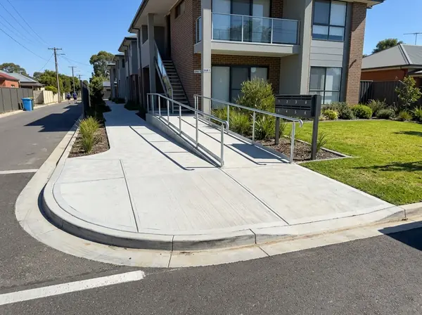 Wide concrete footpath and ramp with a handrail at a block of units