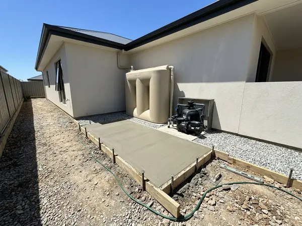 Small concrete pad with a rainwater tank and pool pump on it