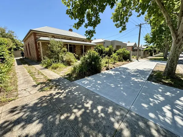 An old narrow cracked strip driveway beside a bluestone villa, next to a neighbour's new full-width exposed aggregate driveway, Unley
