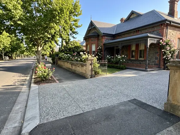 A new exposed aggregate driveway beside a bluestone villa with red brick quoins and a return verandah on a plane-tree street in Unley