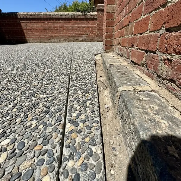 Close up of a new exposed aggregate driveway edge meeting an old bluestone kerb and a red brick wall